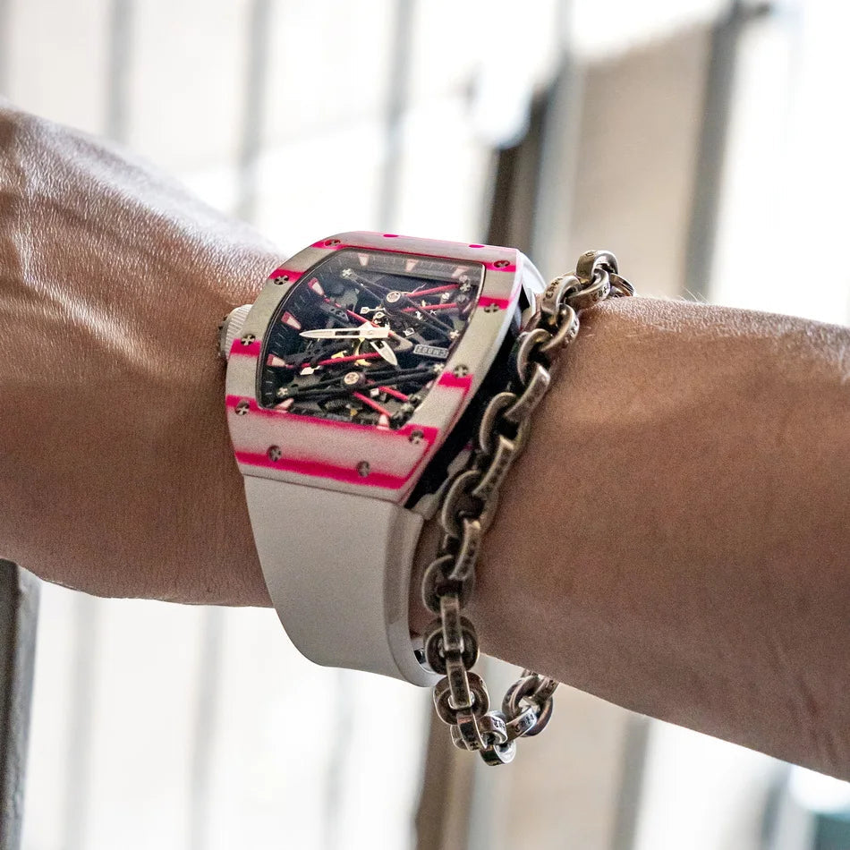 Luxury watch with pink and black design on a wrist, wearing a chain bracelet.