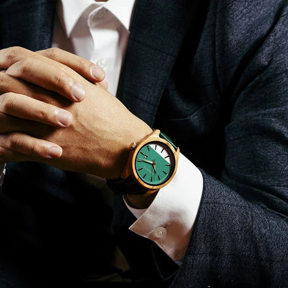 Person wearing a watch with a green face and gold case.