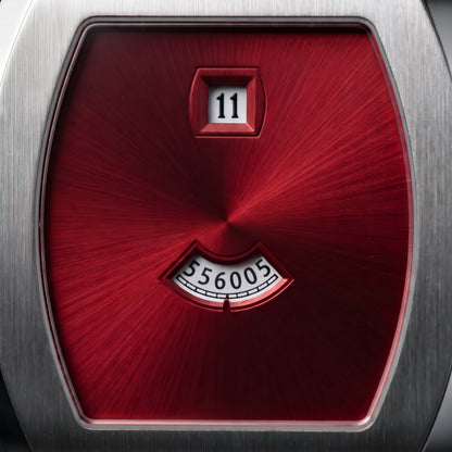 Close-up of a wristwatch dial with a brushed silver metal case and a prominent textured red central face, featuring a date window showing 11 and a small seconds subdial.